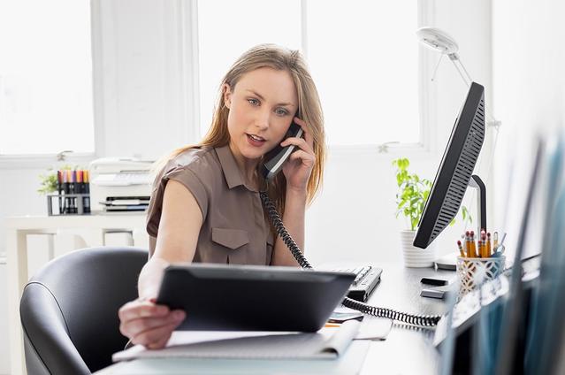 אישה במשרד, מביטה במסך טאבלט ומדברת בטלפון